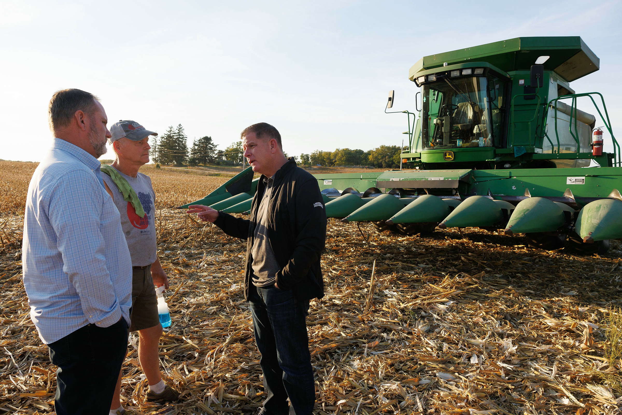 Officials talk with a farmer next to a combine during a farm visit
