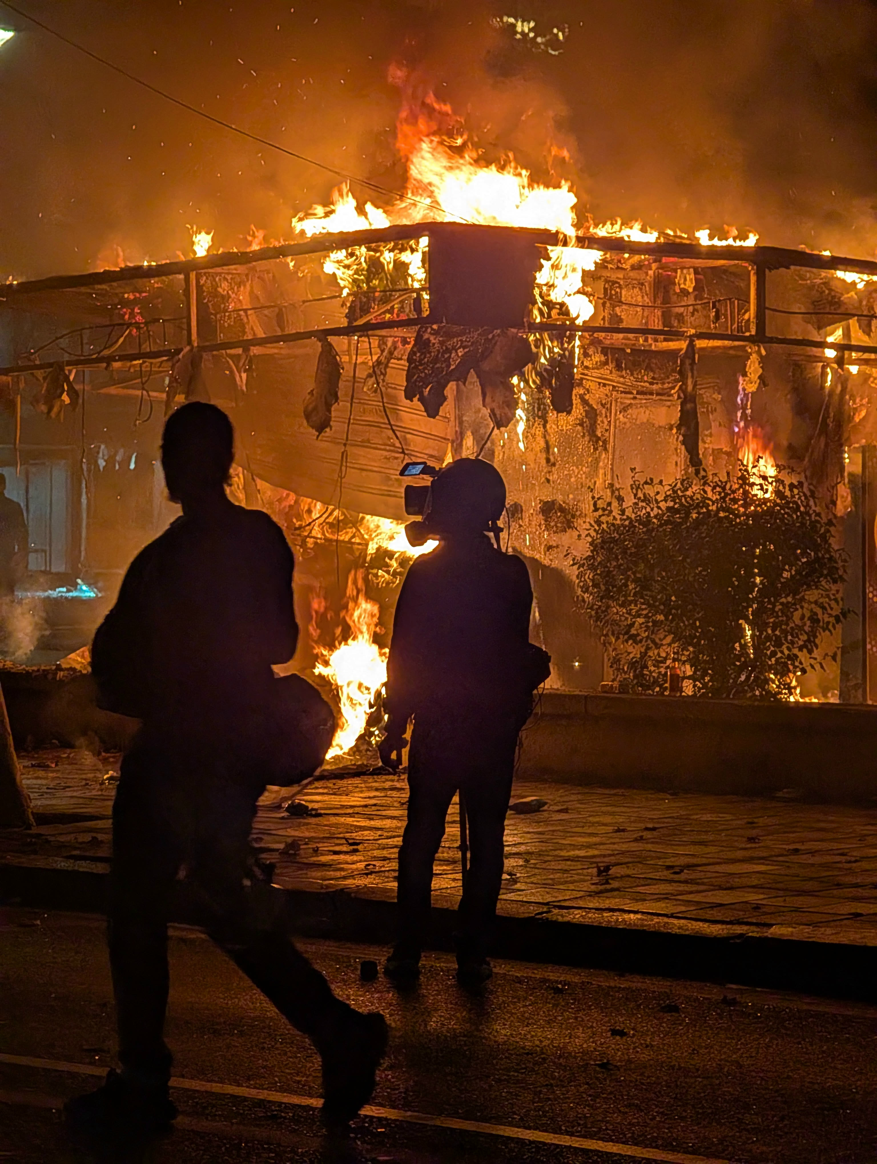 Two people in front of a burning structure during the Tirana protests