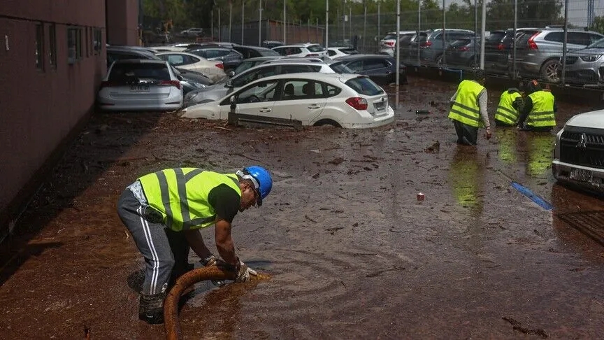 Workers pump out mud among submerged cars in a parking lot in Las Condes