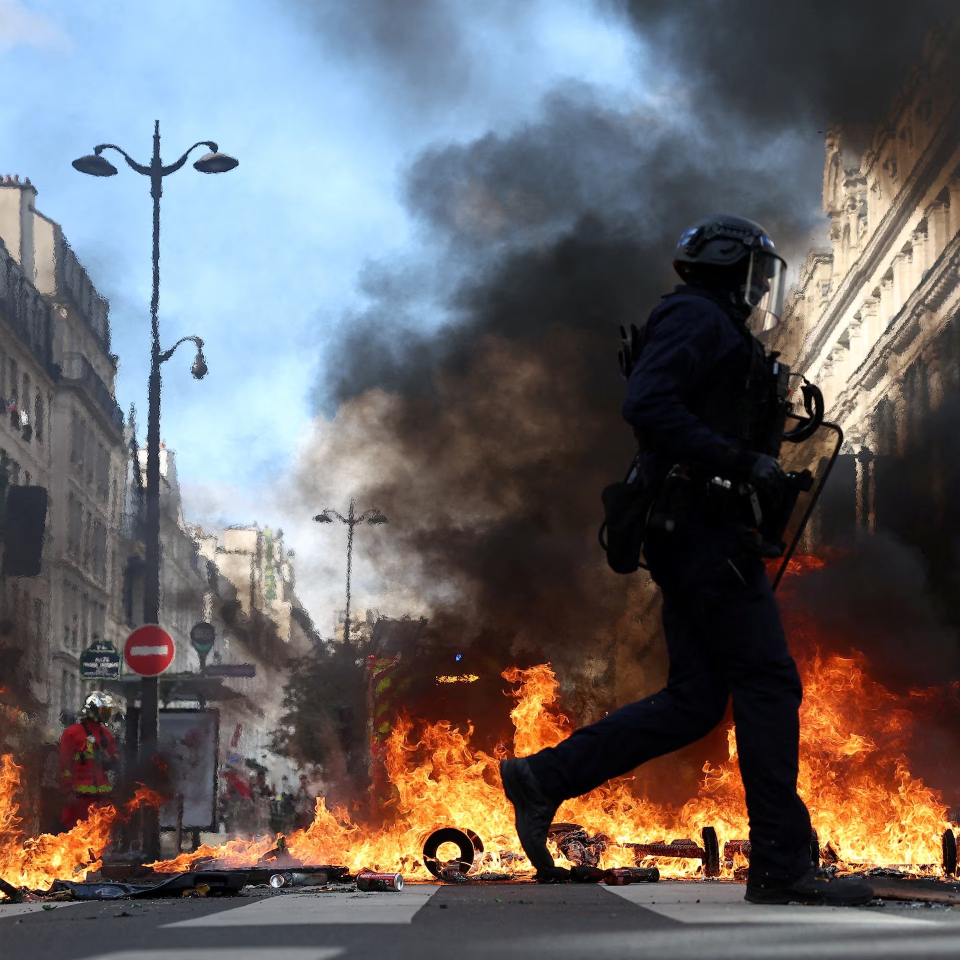 Paris'teki protestolar sırasında yanan barikatların önünden geçen polis memuru